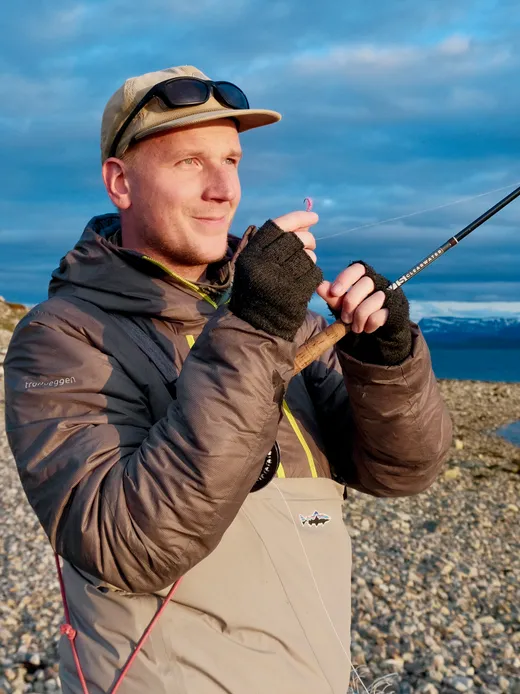 Tommi Heinonen tying on a fly, a Norwegian fjord and snowy mountains behind